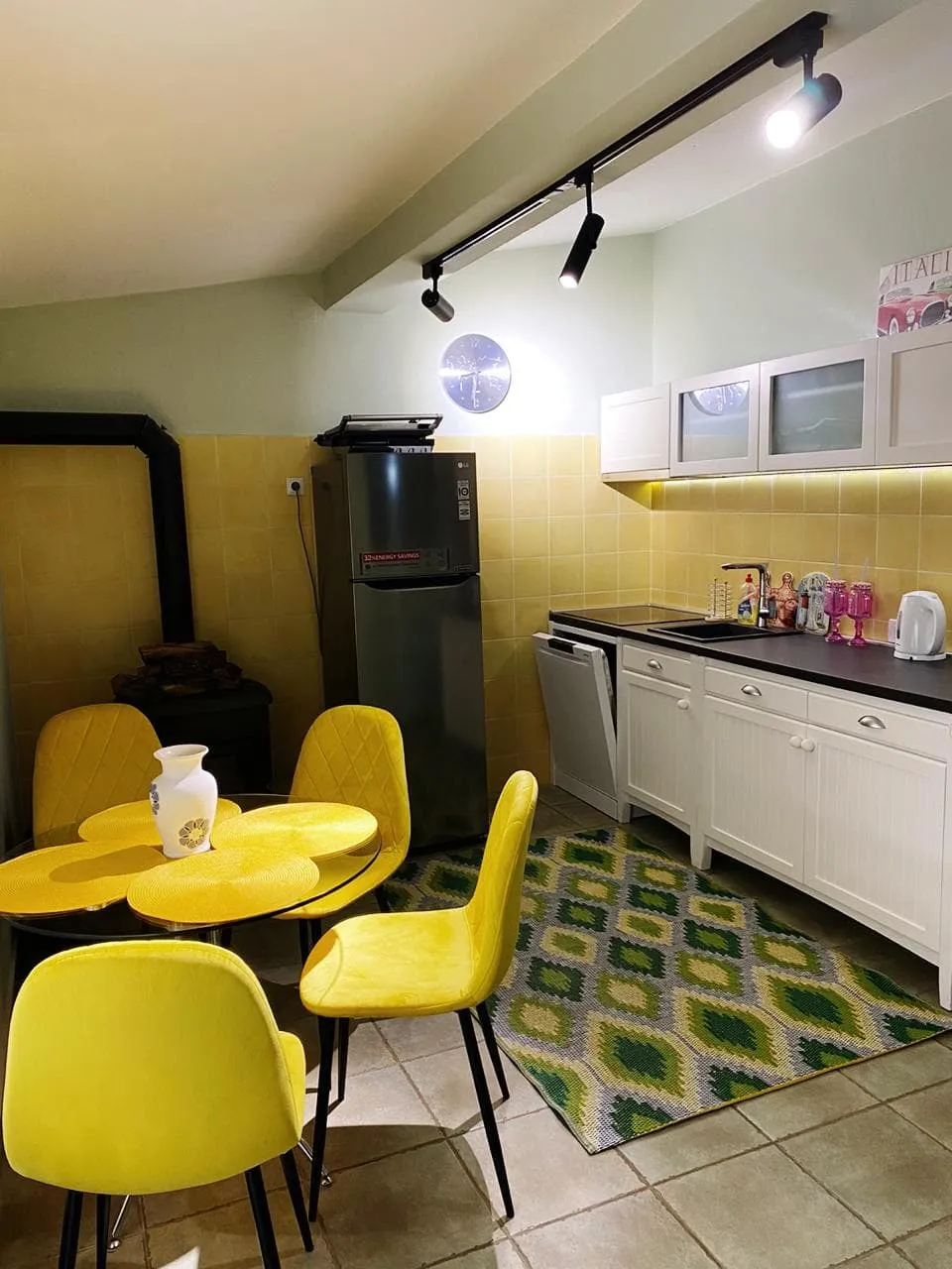 Kitchen with yellow chairs, refrigerator, white cabinets, and black countertop with sink.