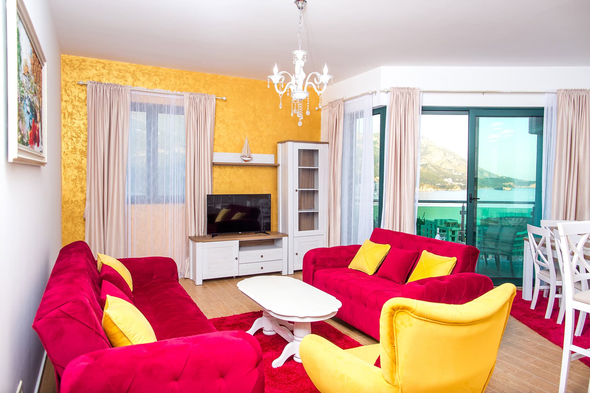 Wohnzimmer mit farbenfrohen Möbeln und Meerblick in einer Wohnung in Bečići, Montenegro: rote Sofas, gelber Sessel und Terrasse.
