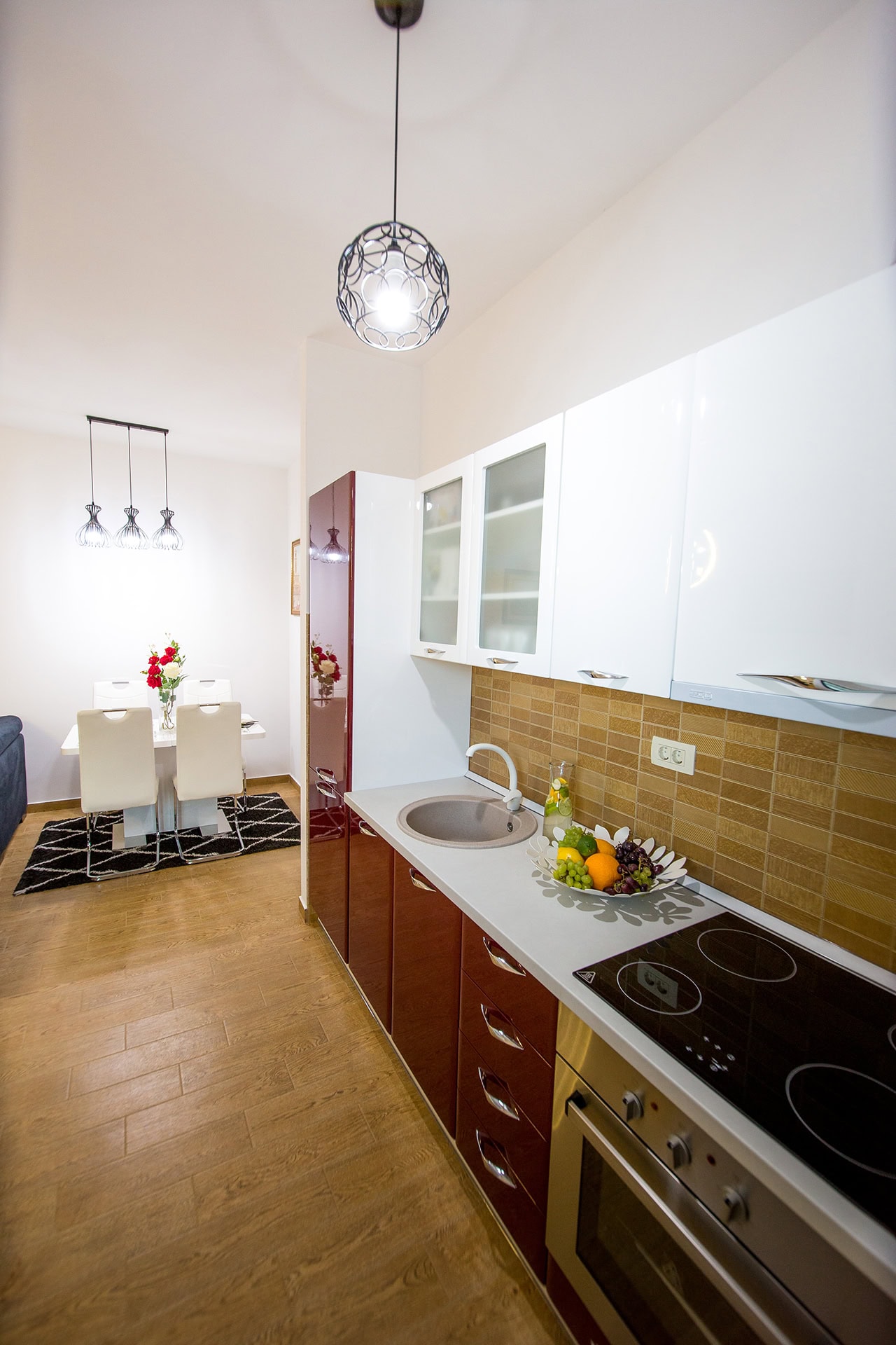 Moderne Küche mit weißen und weinroten Fronten in einer Wohnung in Bečići, Montenegro, kombiniert mit einem Essbereich.