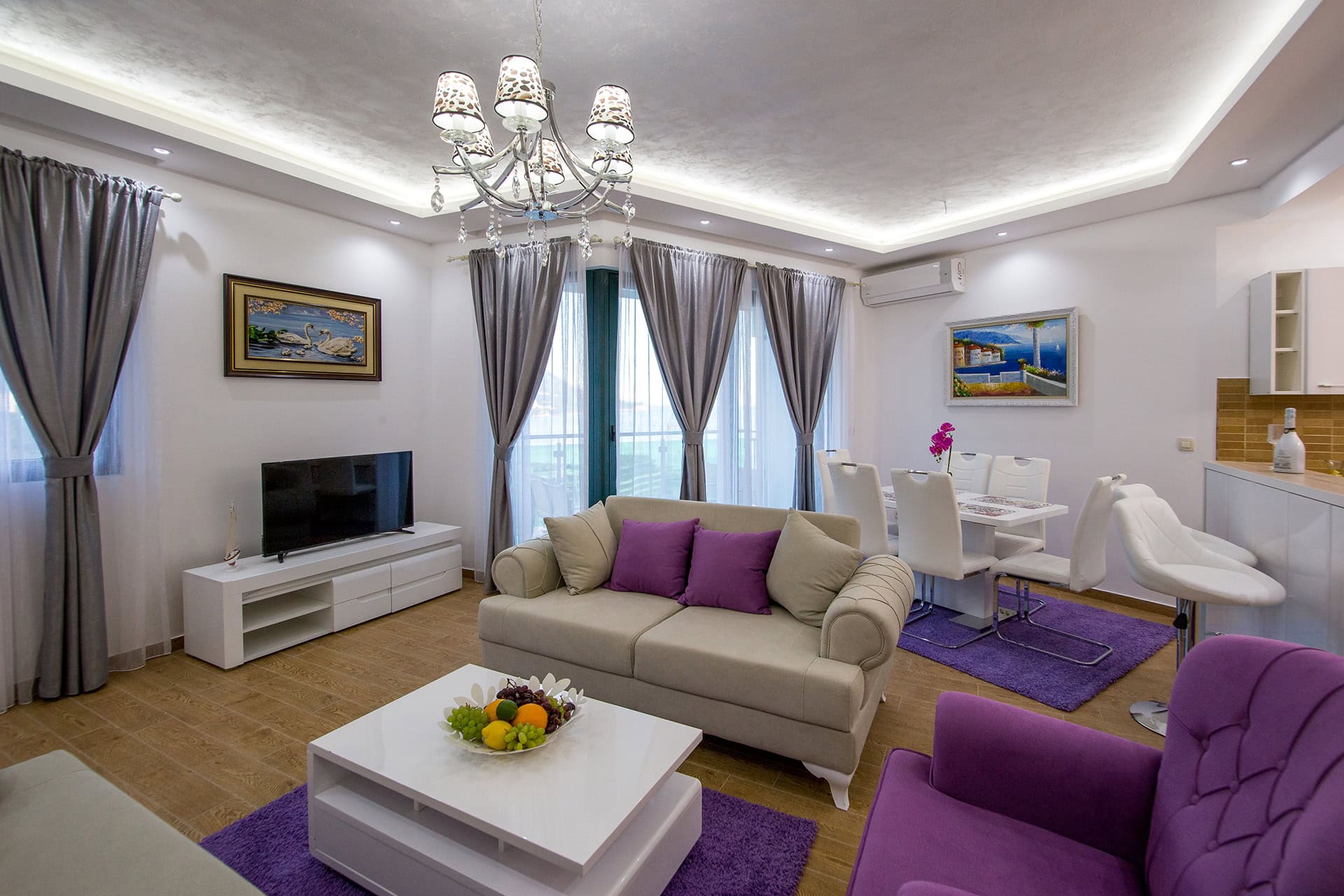 Modernes Wohnzimmer mit violetten Akzenten in einem Apartment, Bečići, Montenegro: Polstermöbel, Essbereich und TV.