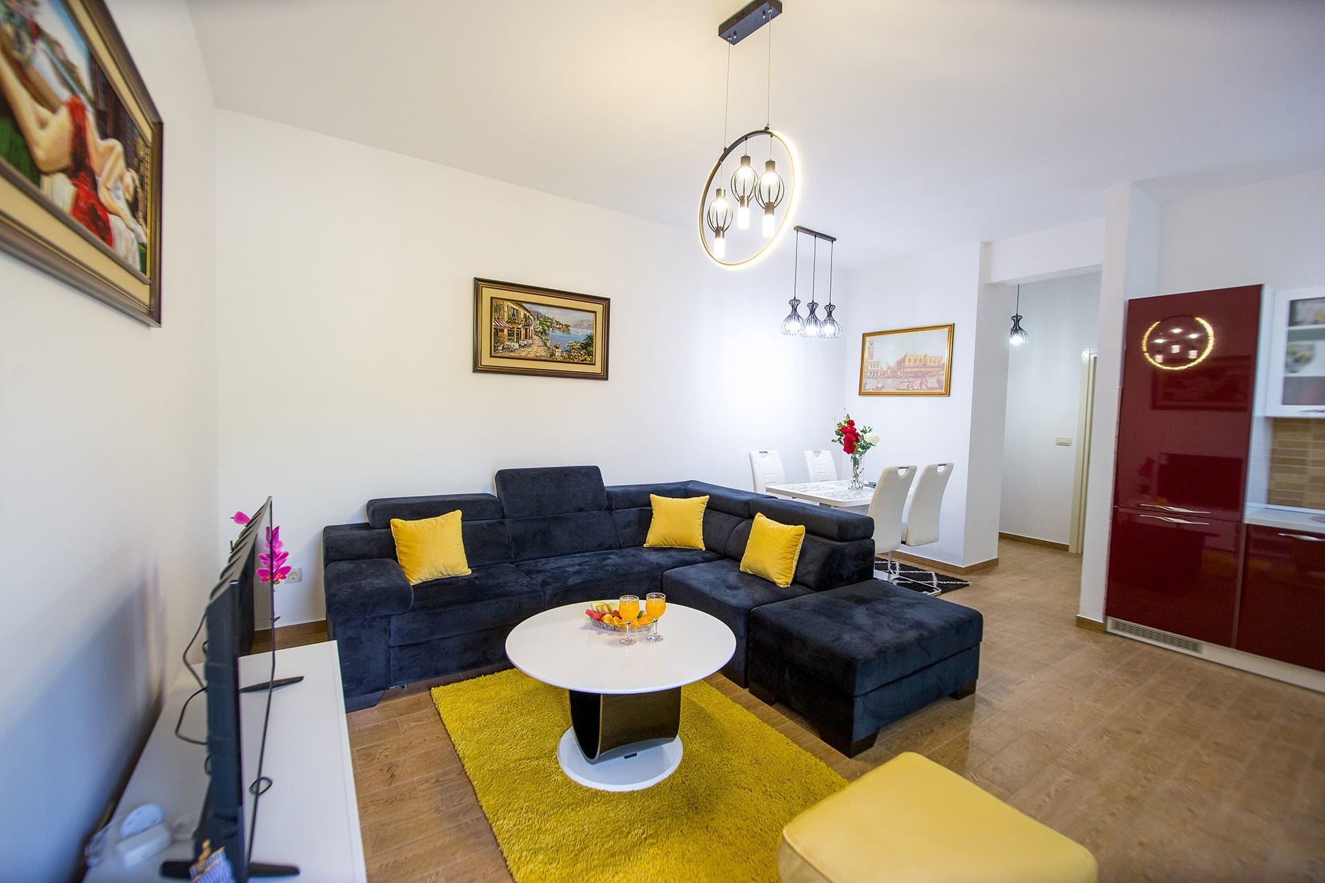 Wohnzimmer mit dunkelblauem Ecksofa und gelber Dekoration in einer Wohnung in Bečići, Montenegro, kombiniert mit einer Küche.