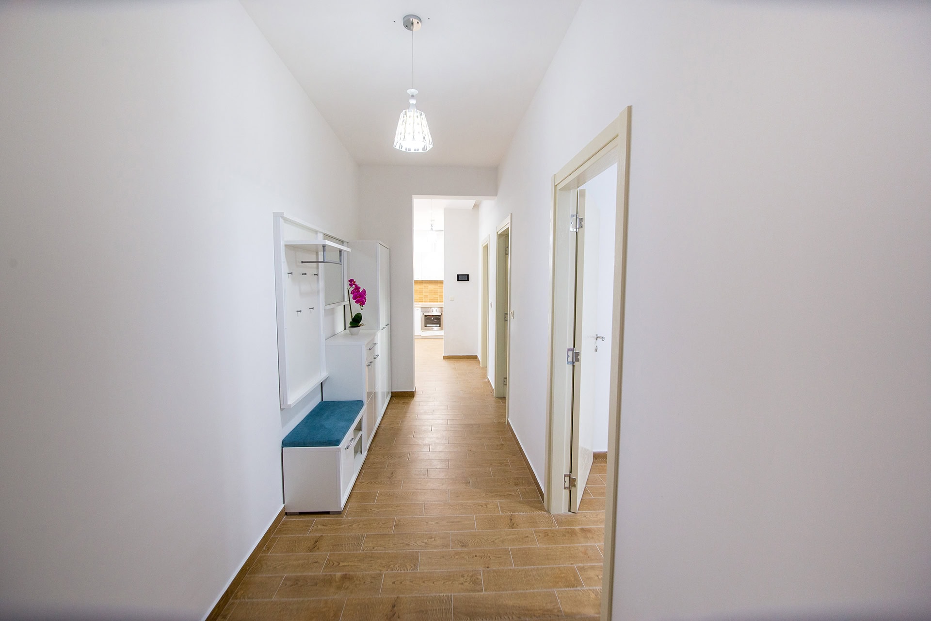 Heller Flur in einer Wohnung in Bečići, Montenegro: weiße Möbel, Fliesen in Holzoptik und Blick auf die moderne Küche.