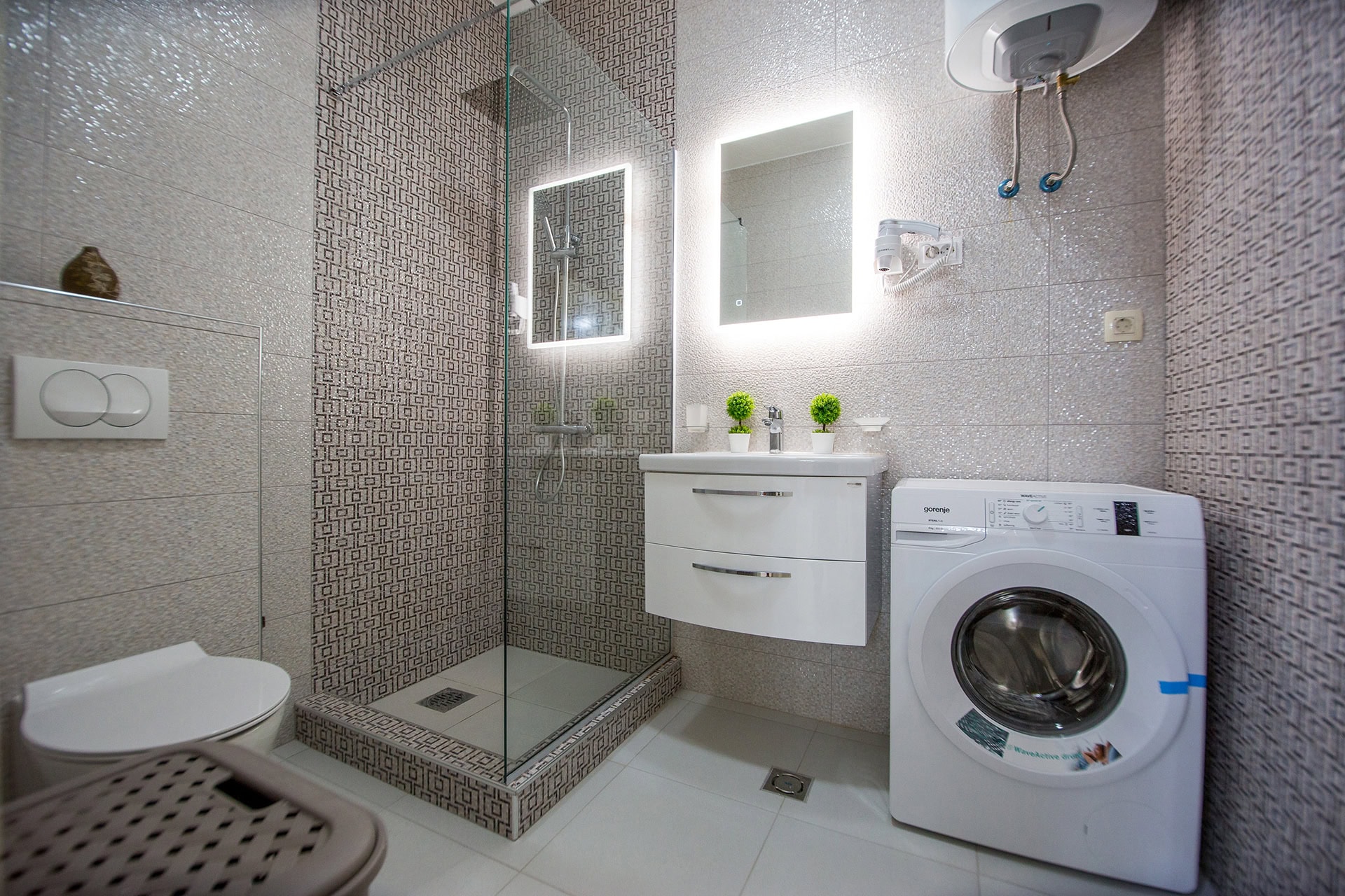 Modernes Badezimmer in einem Apartment in Bečići, Montenegro: Duschkabine, Waschmaschine und beleuchteter Spiegel.