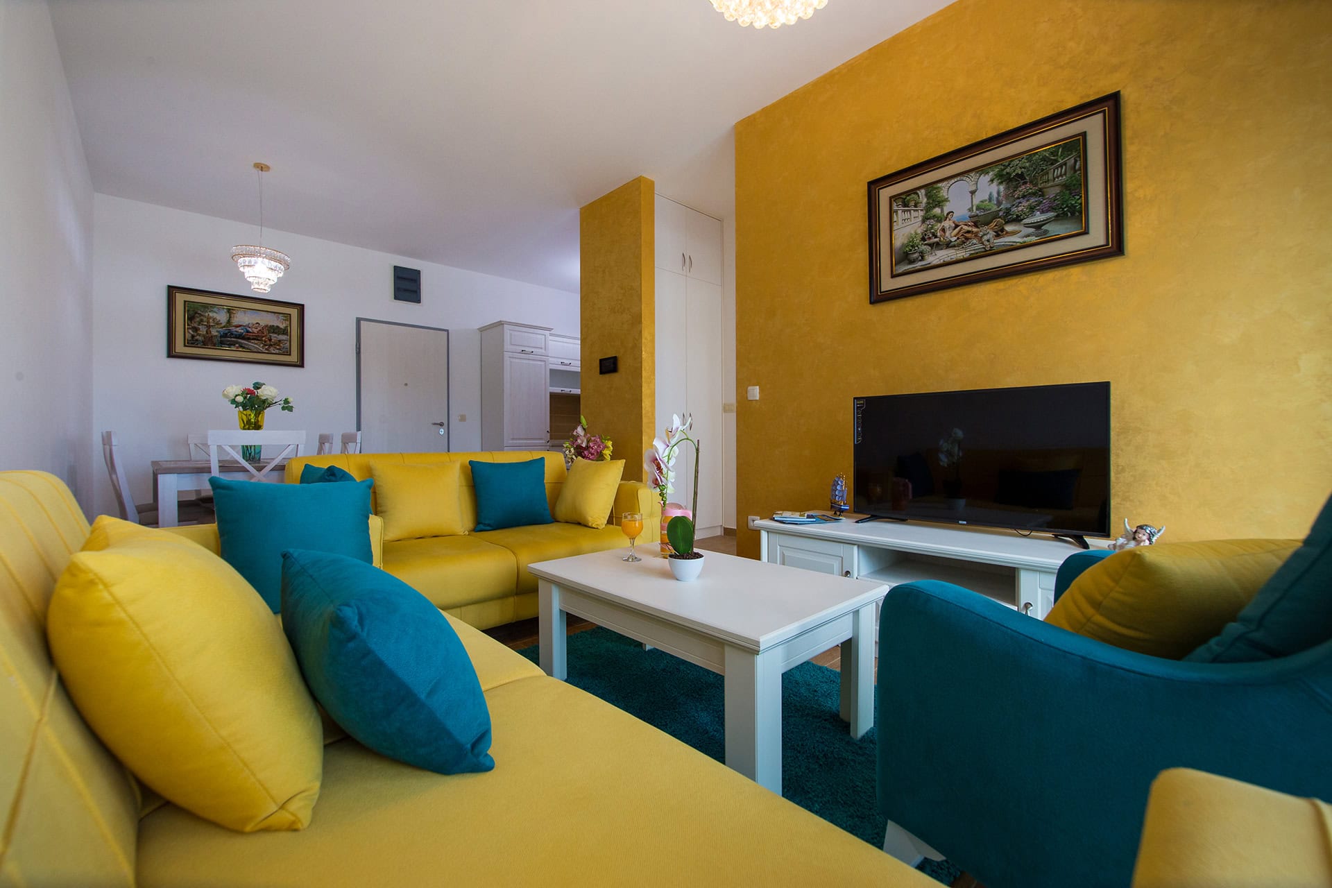 Helles Wohnzimmer mit gelben Wänden, Polstermöbeln und Essbereich in einer Wohnung in Bečići, Montenegro.