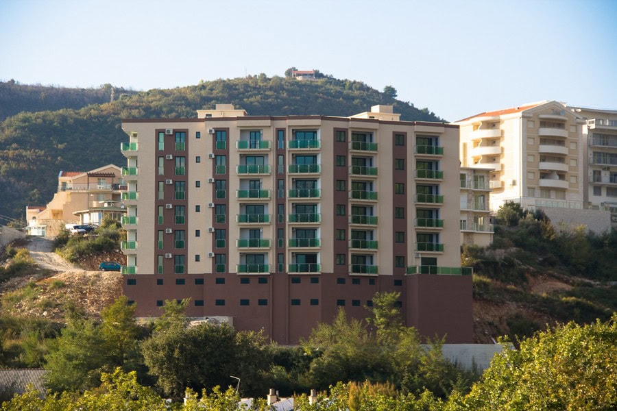 Moderner Wohnkomplex mit Balkonen in Bečići, Montenegro: Blick auf ein mehrstöckiges Gebäude inmitten von Bergen und viel Grün.