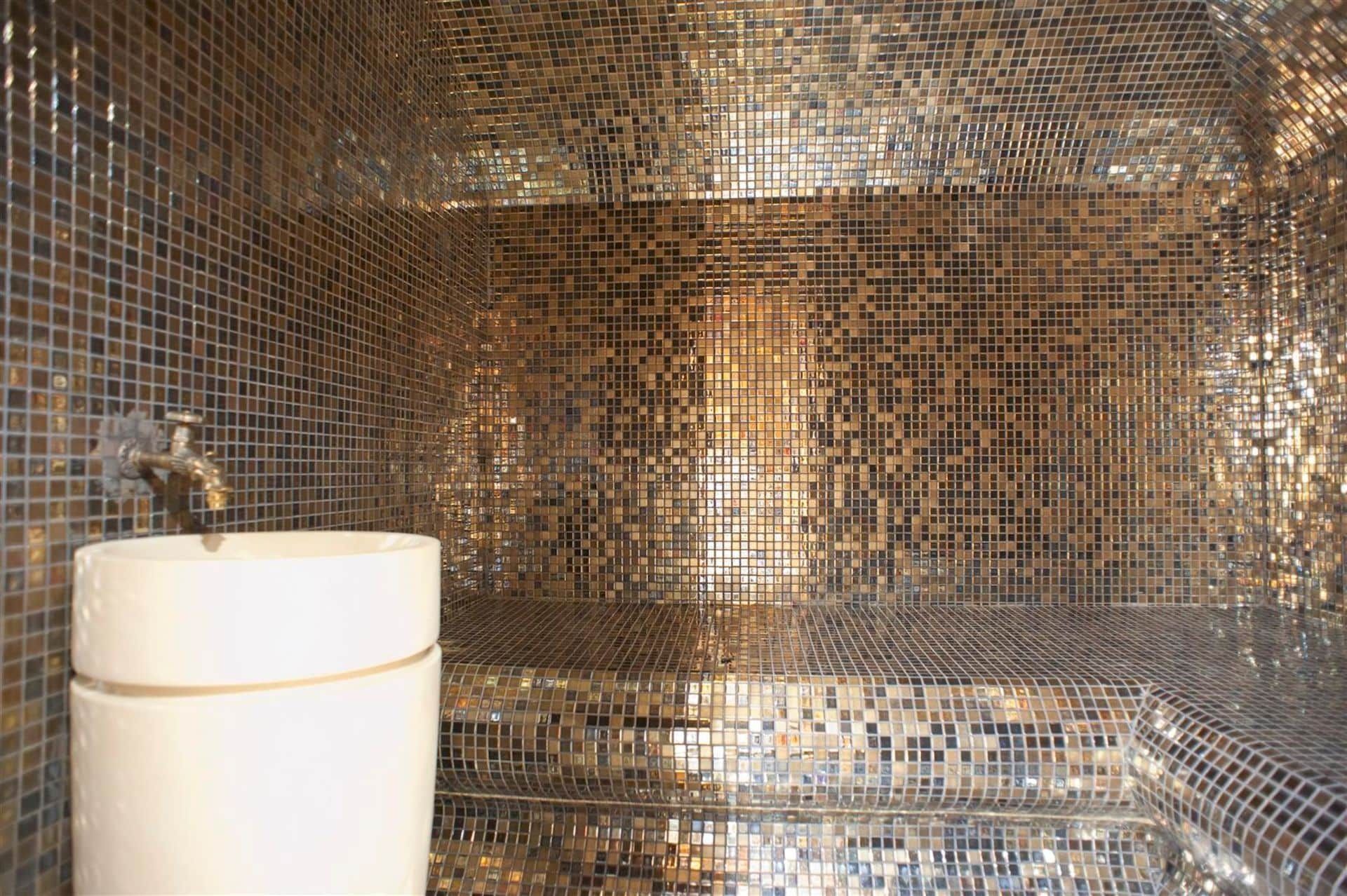 Salle de bains design avec finition en mosaïque dorée et lavabo blanc dans une villa à Krašići, Monténégro.