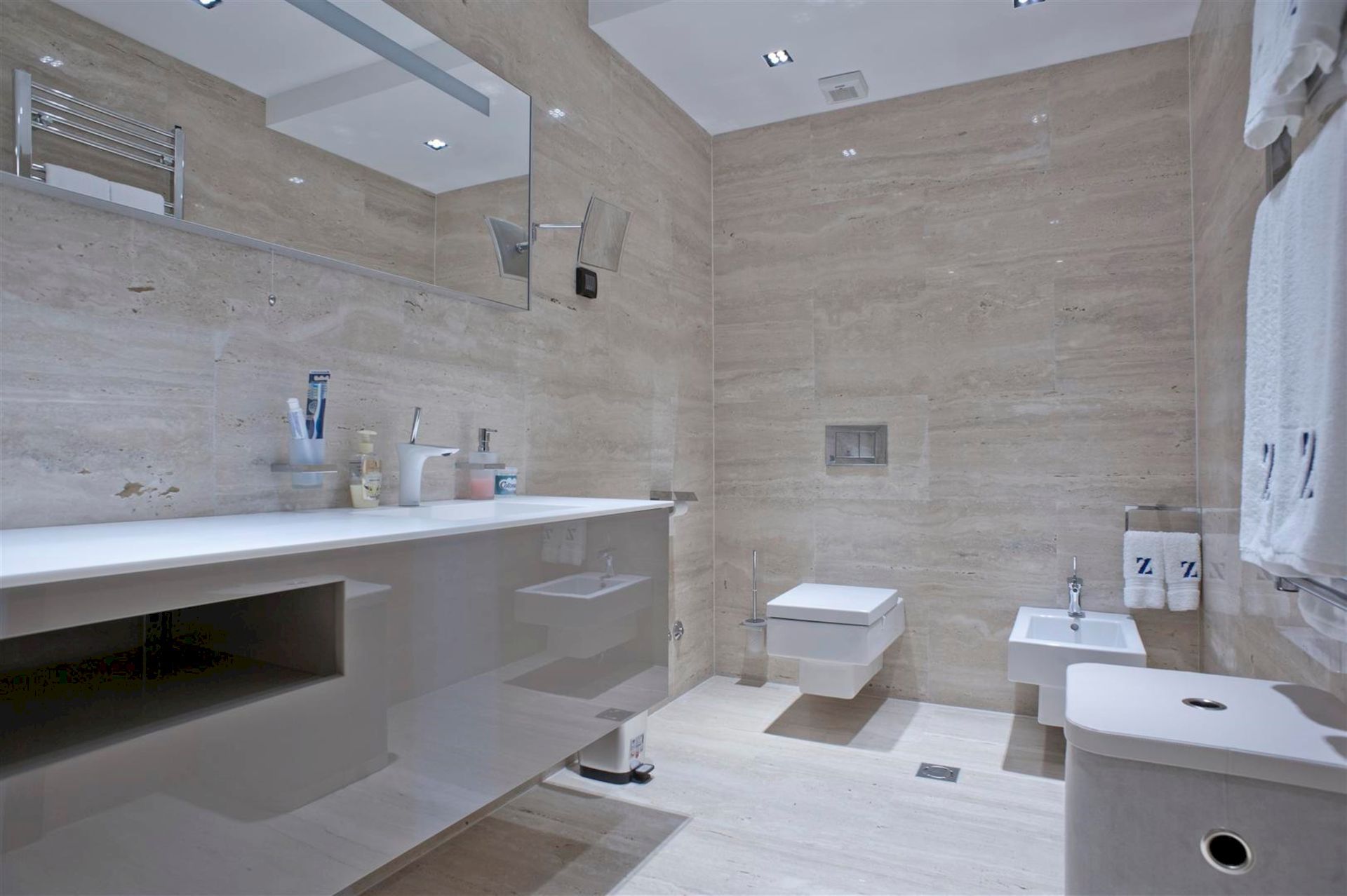 Salle de bains moderne avec finition en pierre beige, sanitaires suspendus et miroir dans une villa à Krašići, Monténégro