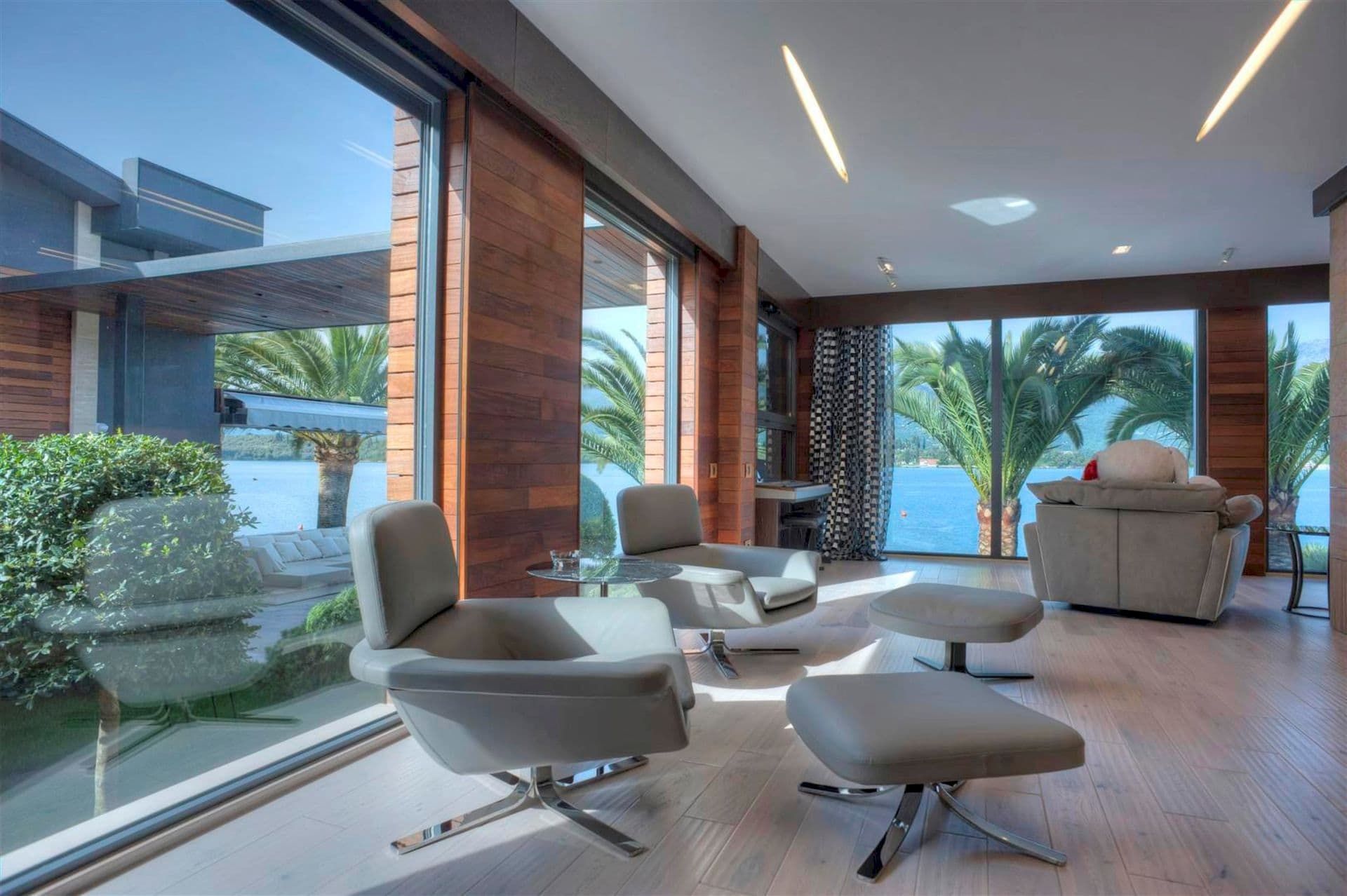 Salon d’une villa moderne à Krašići, Monténégro : baies vitrées panoramiques, vue sur la mer, finitions en bois et mobilier élégant.