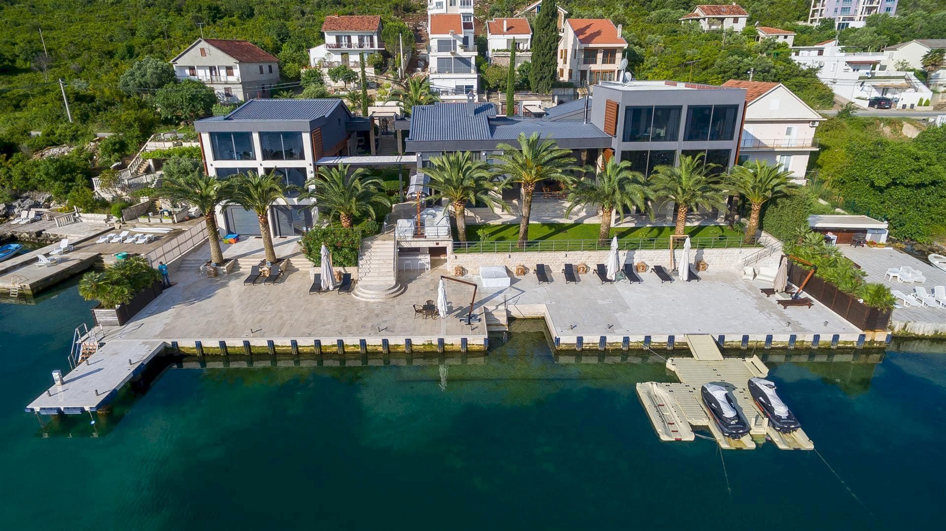Villa moderne à Krašići, Monténégro : vue panoramique sur la maison avec son propre ponton, sa plage et des palmiers au bord de la mer.