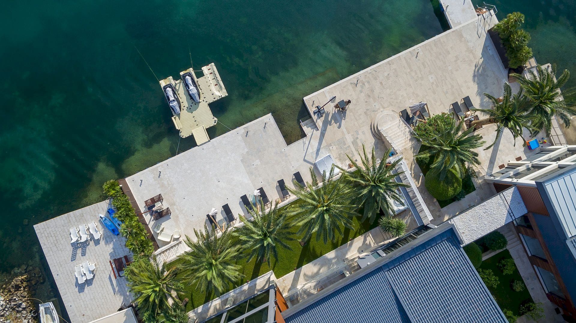 Vue aérienne d’une villa à Krašići, Monténégro : plage privée, ponton pour bateaux, transats et palmiers au bord de la mer.