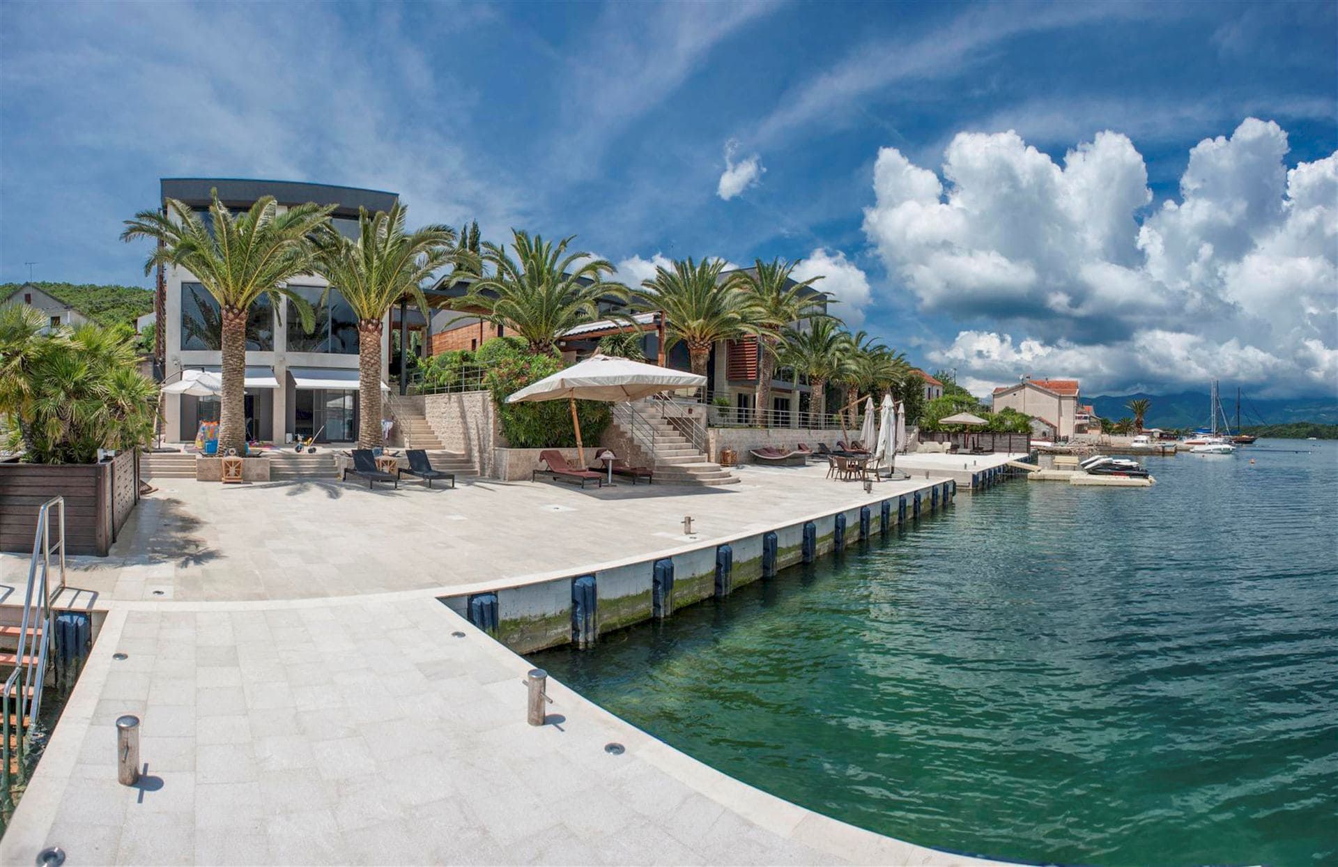 Villa moderne à Krašići, Monténégro : quai privé, terrasse avec chaises longues, palmiers et accès direct à la mer.