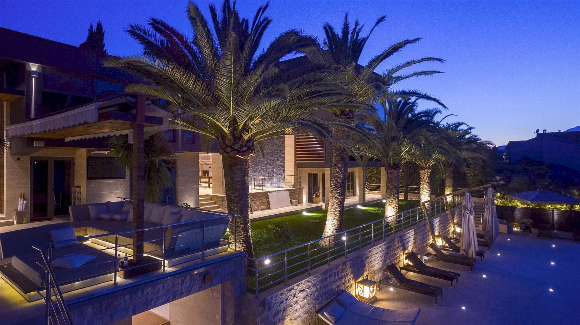 Villa du soir à Krašići, Monténégro : terrasse avec mobilier moelleux, palmiers, éclairage et espace détente au bord de la piscine.
