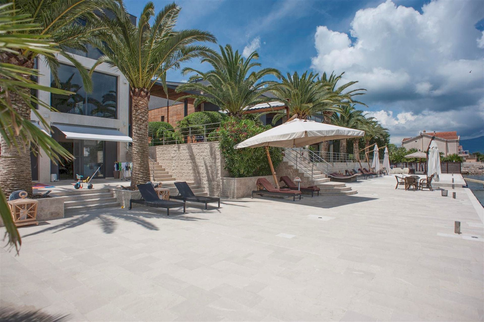 Terrasse d’une villa moderne à Krasići, Monténégro : transats, palmiers et accès direct à la mer depuis une plage privée.