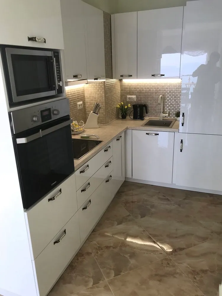 Modern white kitchen in an apartment in Dobri Vody, Montenegro: built-in appliances, glossy fronts, and tile.