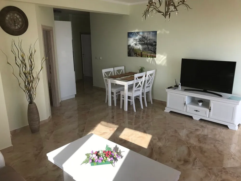 Bright living room with dining area in an apartment, Dobri Vody, Montenegro: white furniture, tiled floor, and TV area.