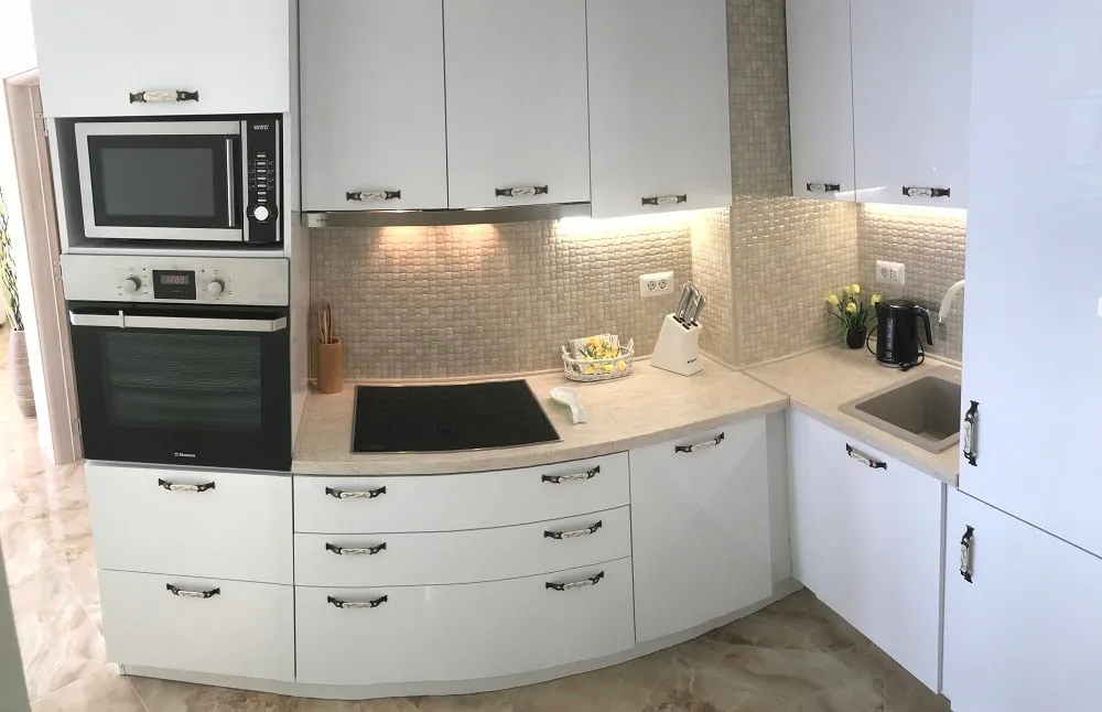 Modern white kitchen with built-in appliances in an apartment, Dobri Vody, Montenegro: stove, oven, and mosaic backsplash.