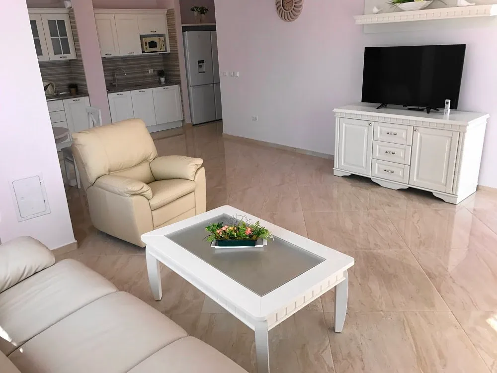 Bright living room with kitchen in an apartment in Dobri Vody, Montenegro: white furniture, leather armchair, and marble floor.