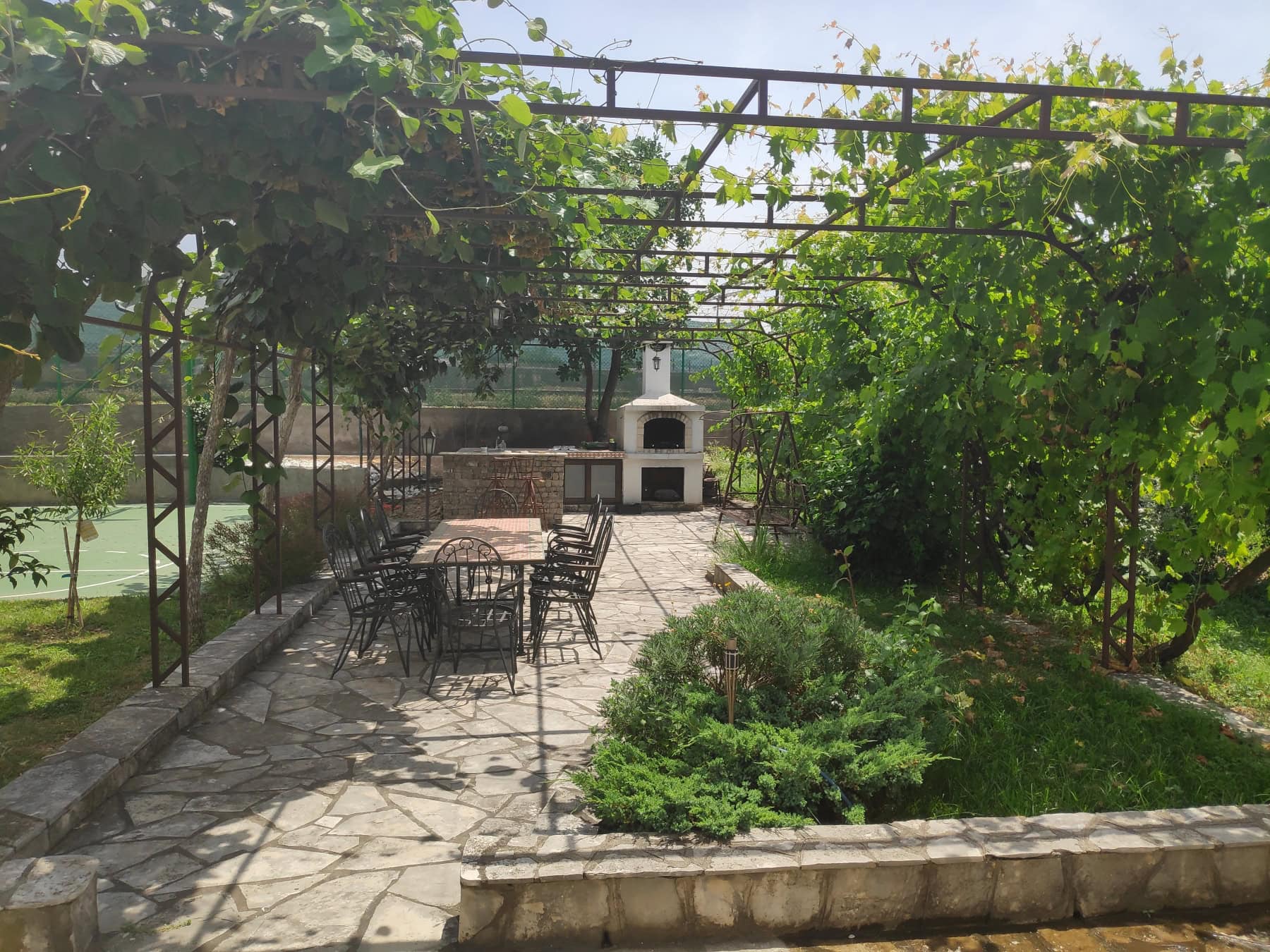 Karadağ, Bar şehrindeki evin уютlu bahçesinde taş mangallı barbekü alanı ve bahçe mobilyaları.