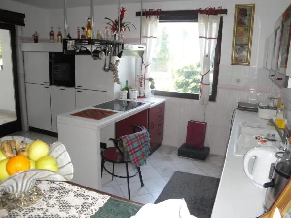 A kitchen with a counter, white cabinets, and window with white curtains.