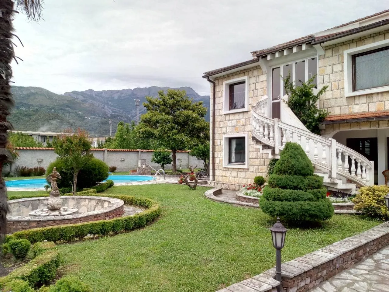 Stone house exterior with a lawn, outdoor stairs, fountain, and swimming pool.