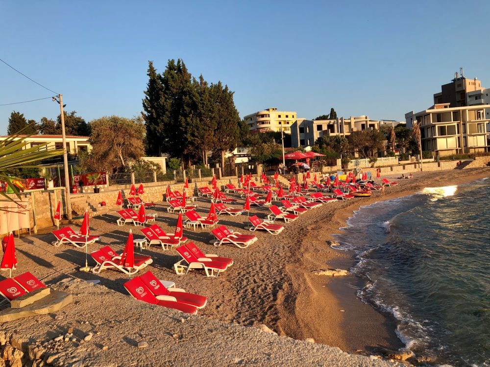 Karadağ, Dobri Vody kasabasında deniz kenarında kırmızı şezlonglar ve şemsiyelerle donatılmış plaj manzarası.