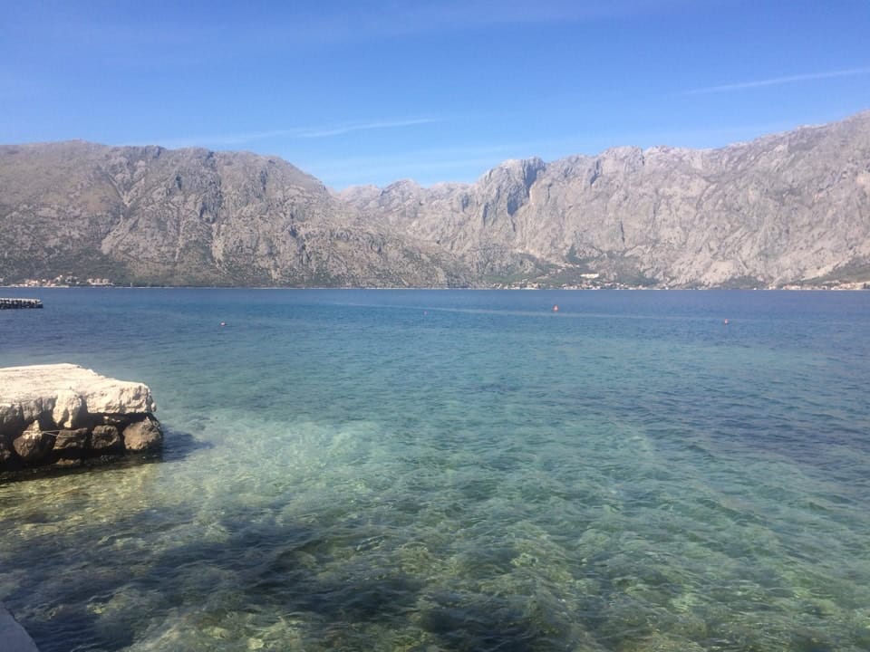 Prčanj, Karadağ’daki daireden Kotor Körfezi ve dağların panoramik manzarası: berrak su ve taş iskele.