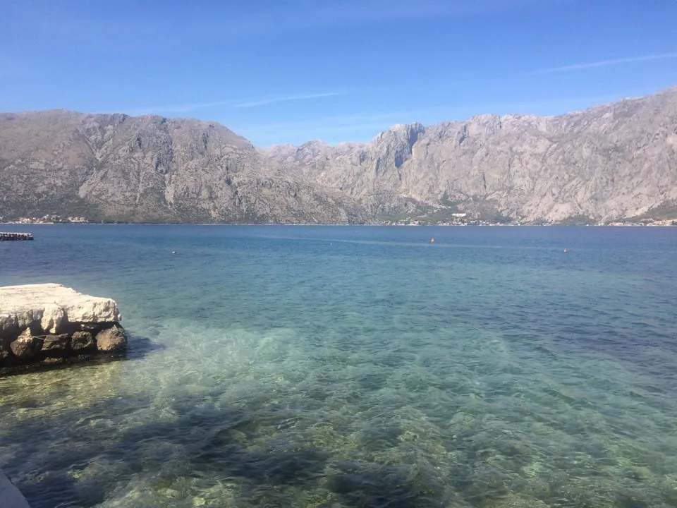 Prčanj, Karadağ’daki daireden Kotor Körfezi ve dağların panoramik manzarası: berrak su ve taş iskele.