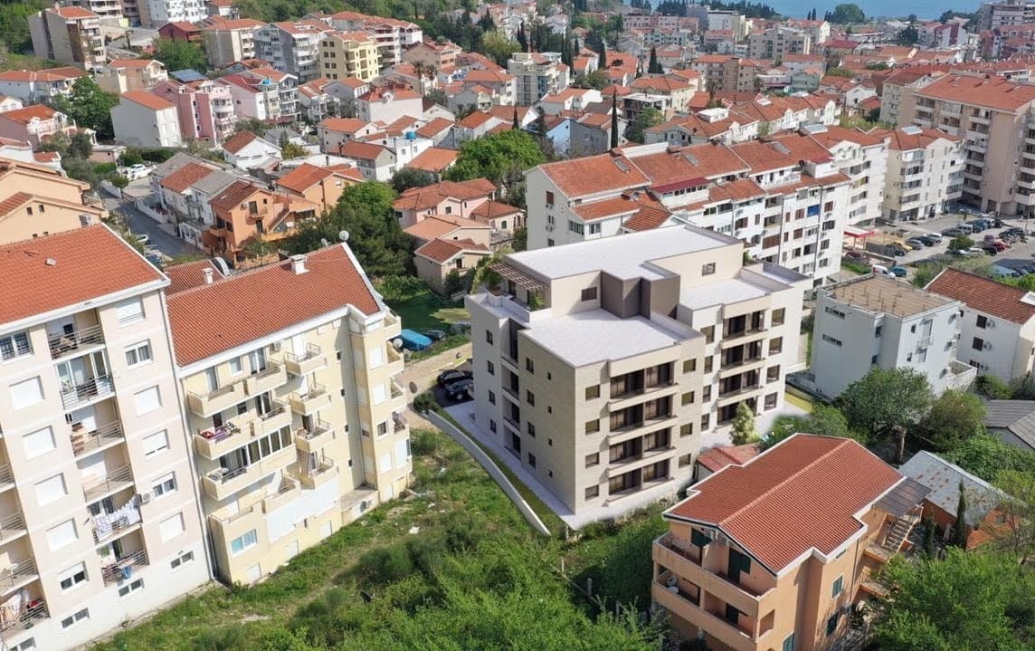 Luftaufnahme eines modernen Wohnkomplexes in Budva, Montenegro, zwischen städtischer Bebauung mit Ziegeldächern.