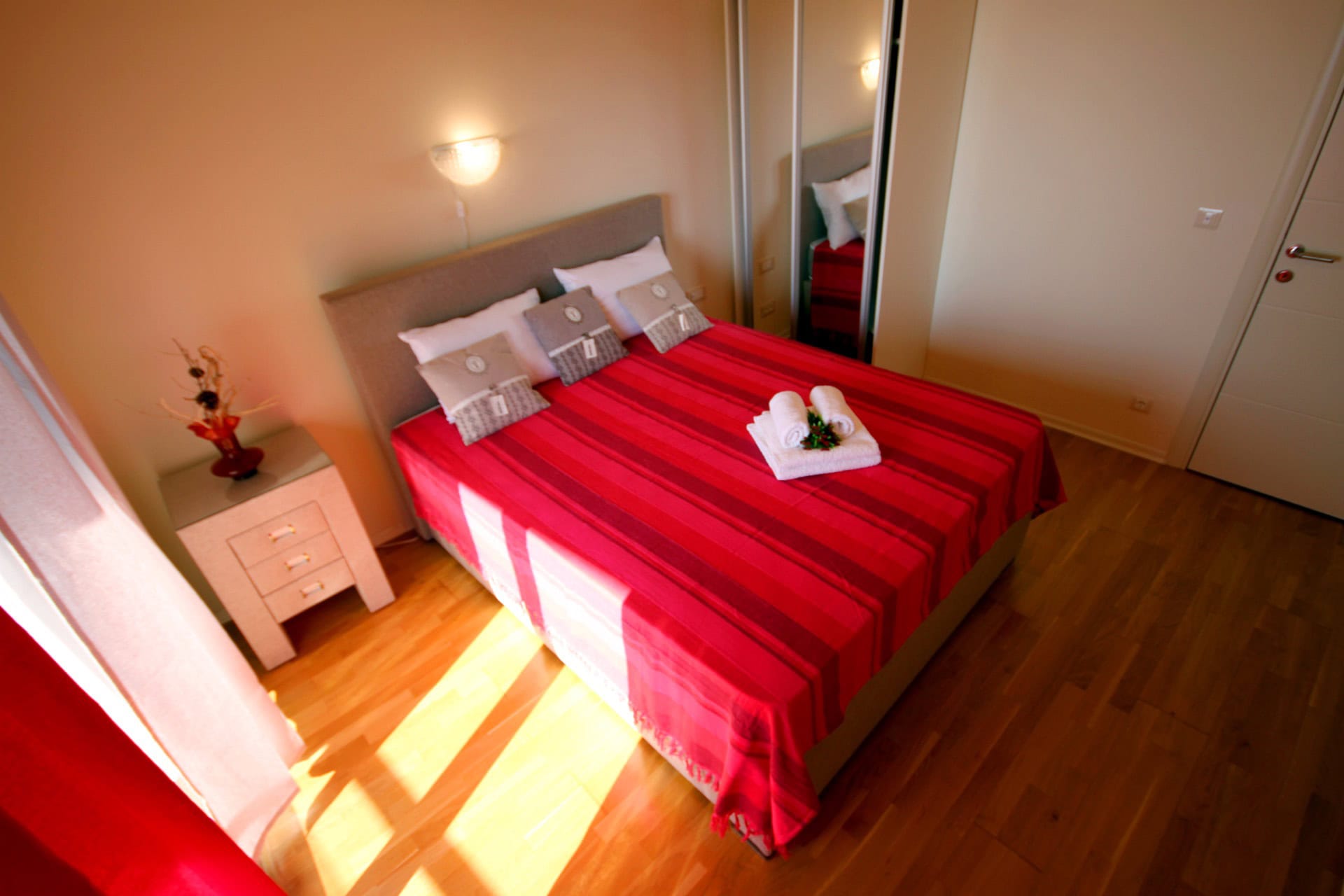 Gemütliches Schlafzimmer mit Doppelbett in einer Wohnung in Bečići, Montenegro: helles Interieur, Parkett und Kleiderschrank mit Spiegeltüren.