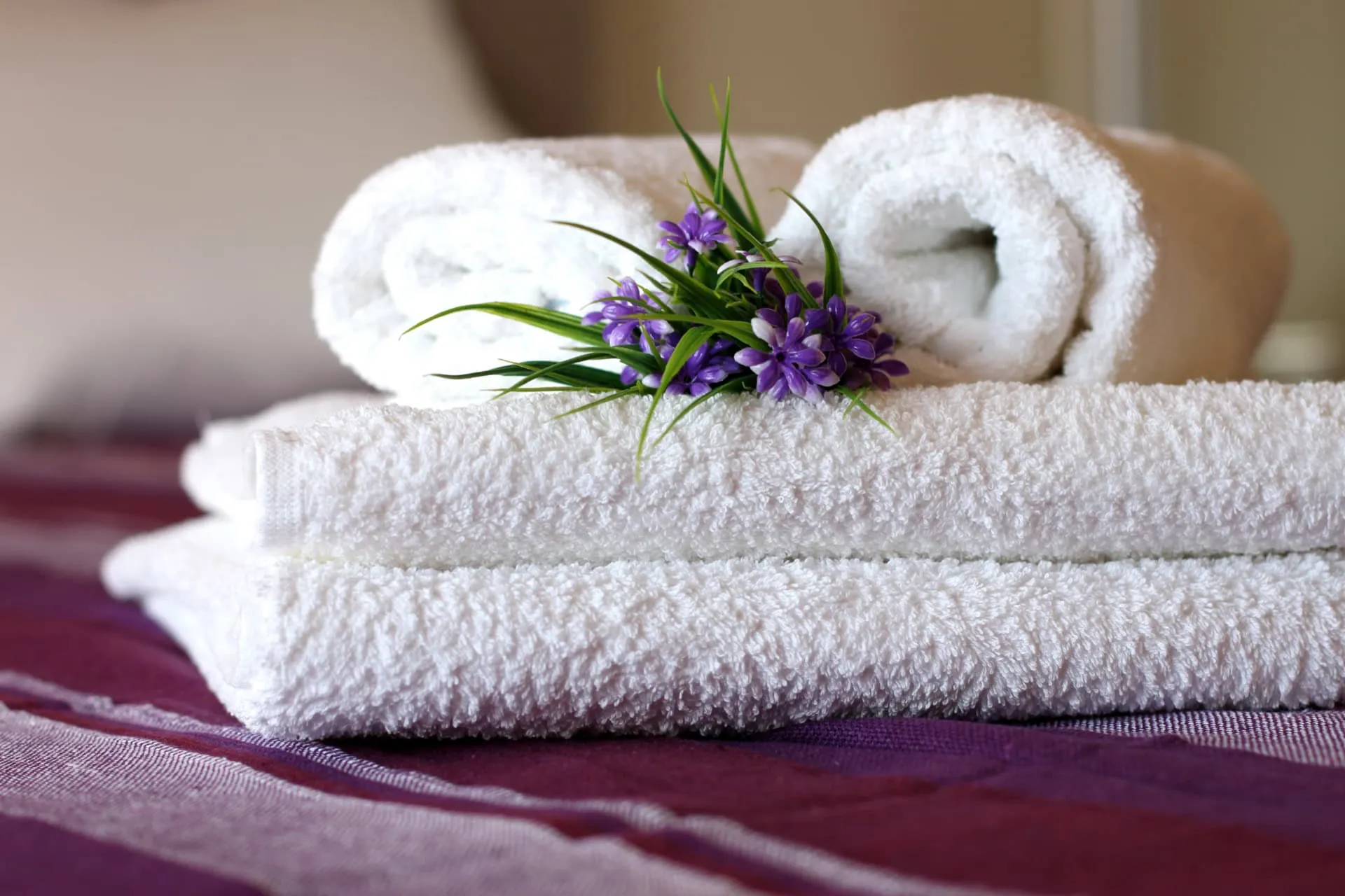 Weiße Frotteehandtücher mit Blumen auf dem Bett im Schlafzimmer der Apartments in Bečići, Montenegro.