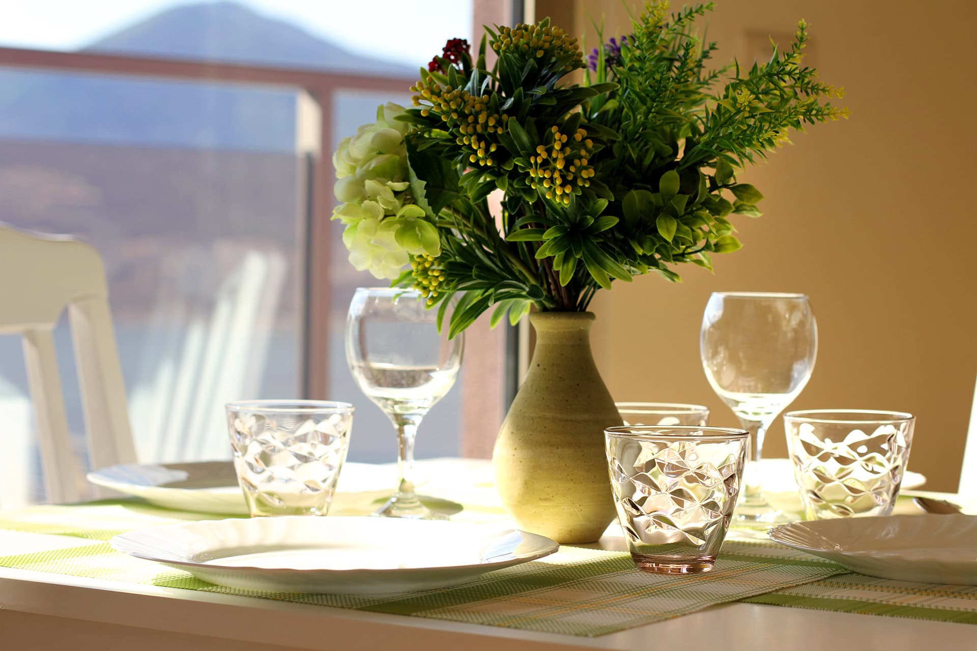 Tischgedeck mit Blumen im Wohnzimmer einer Wohnung in Bečići, Montenegro, mit Bergblick durch ein Panoramafenster.