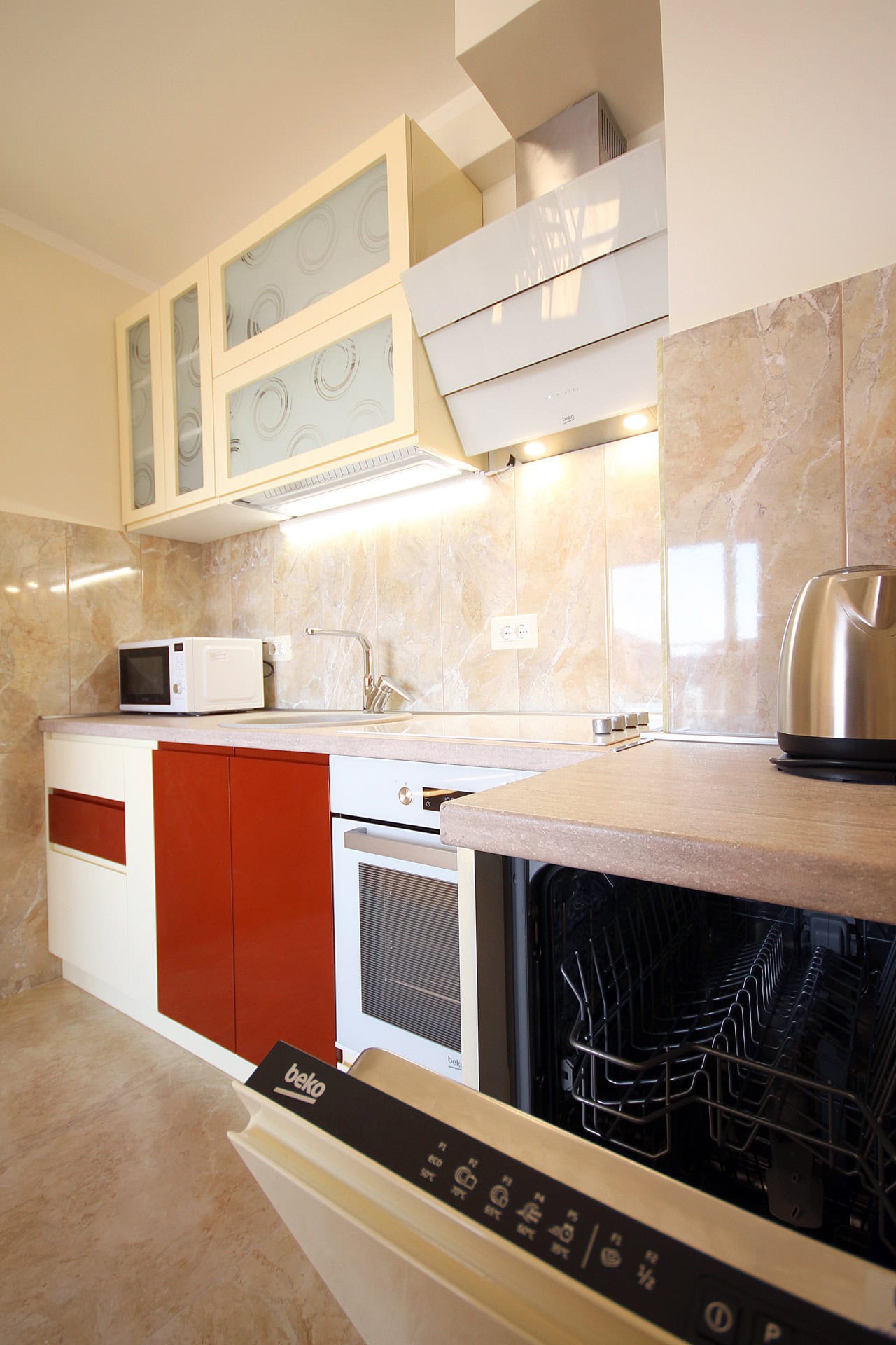Moderne Küche in einer Wohnung in Bečići, Montenegro: eingebaute Beko-Geräte, helle Fronten und Marmor-Spritzschutz.