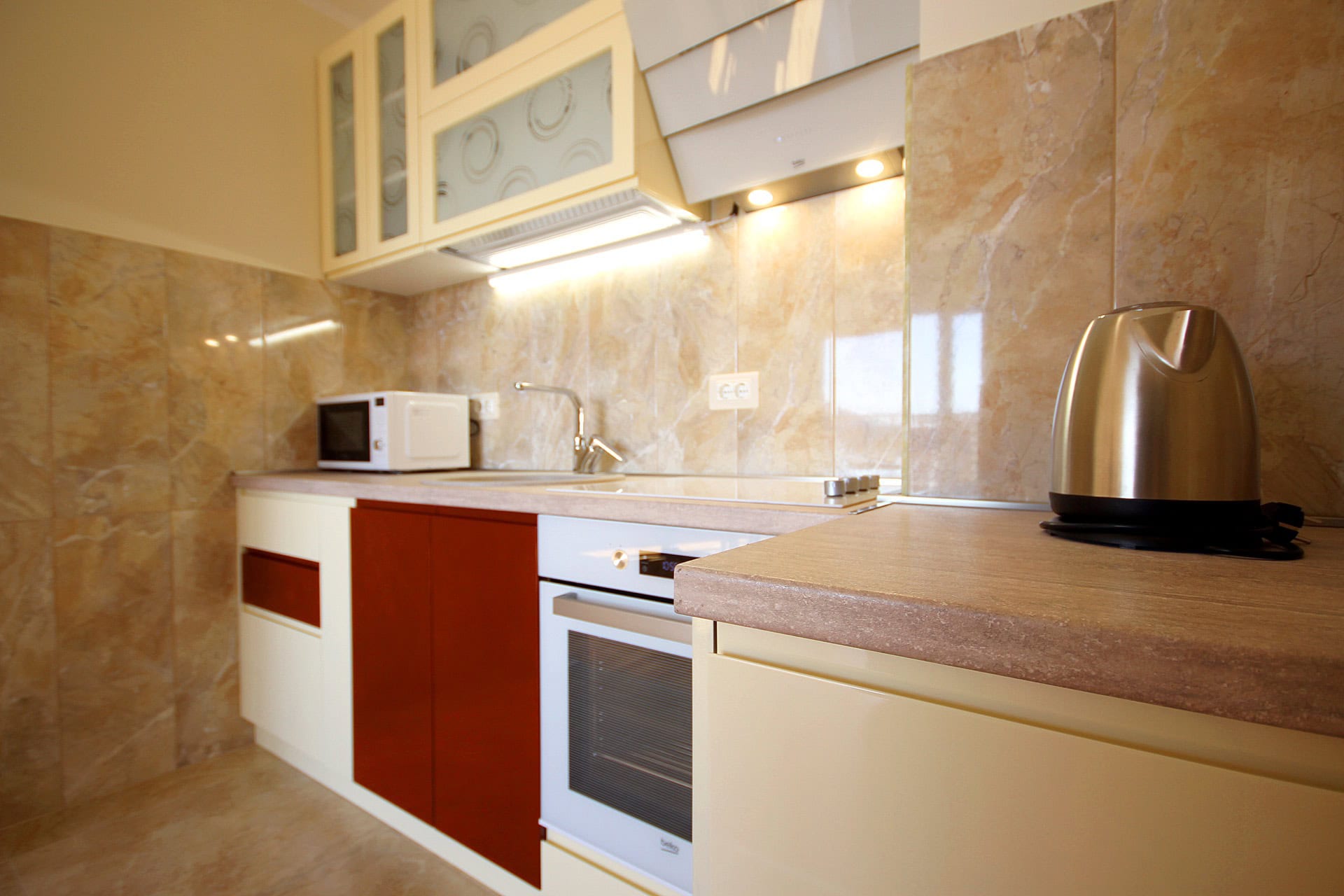 Moderne Küche in einer Wohnung in Bečići, Montenegro: Einbaugeräte, glänzende Fronten und Marmoroptik-Fliesenverkleidung.