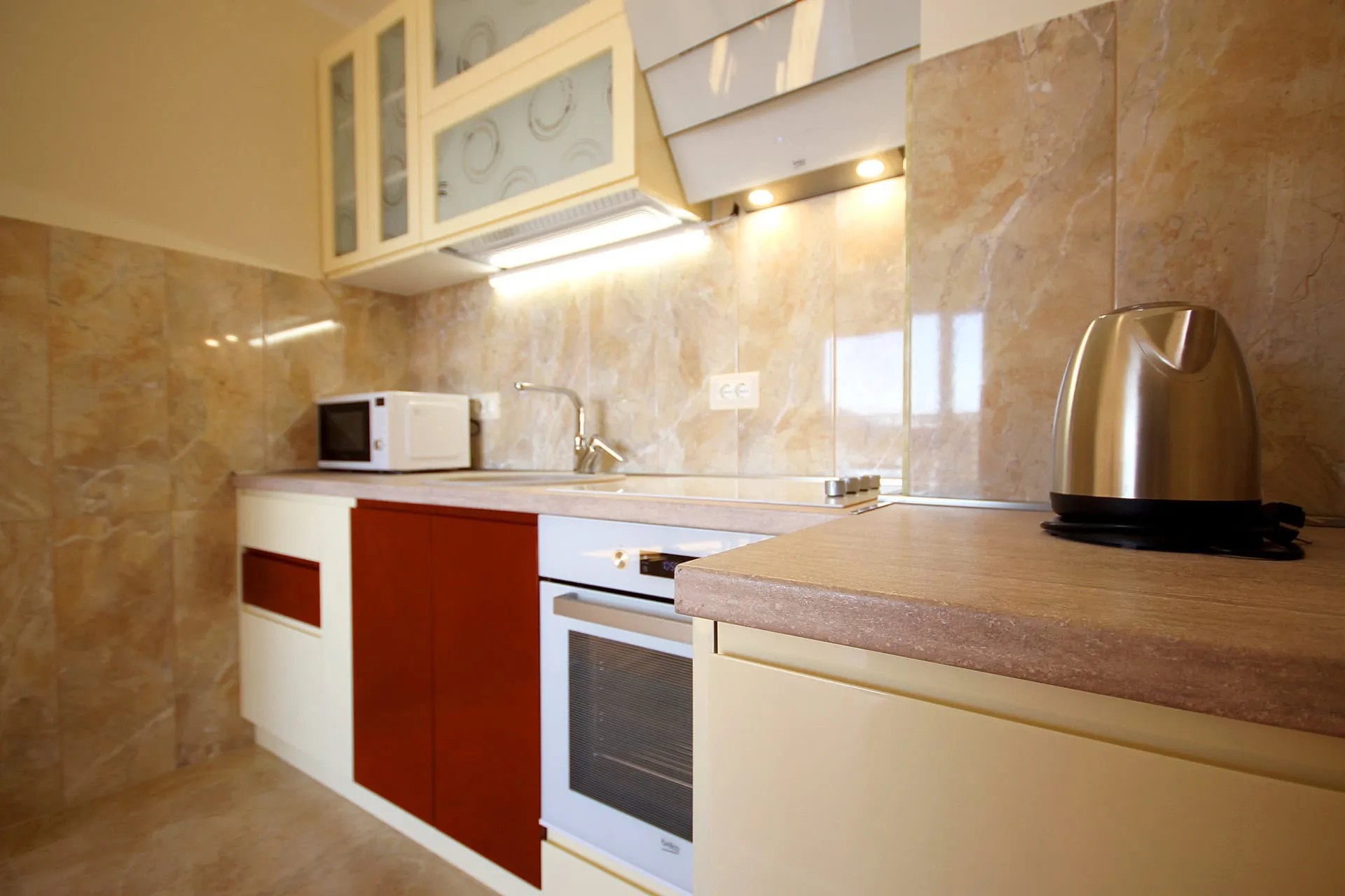 Moderne Küche in einer Wohnung in Bečići, Montenegro: Einbaugeräte, glänzende Fronten und Marmoroptik-Fliesenverkleidung.