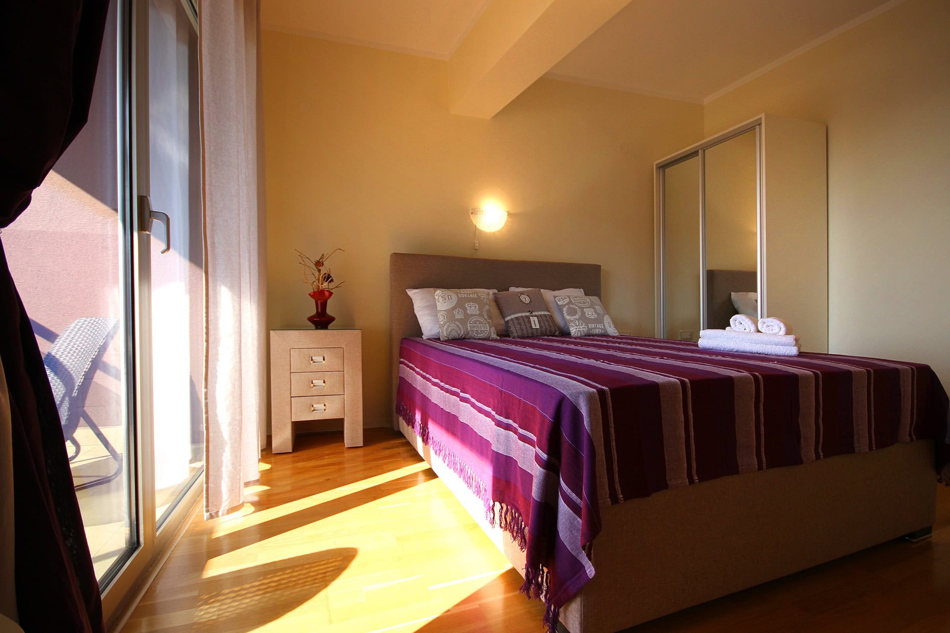 Gemütliches Schlafzimmer mit Doppelbett, Kleiderschrank mit Spiegeltüren und Zugang zur Terrasse in einer Wohnung, Bečići, Montenegro.