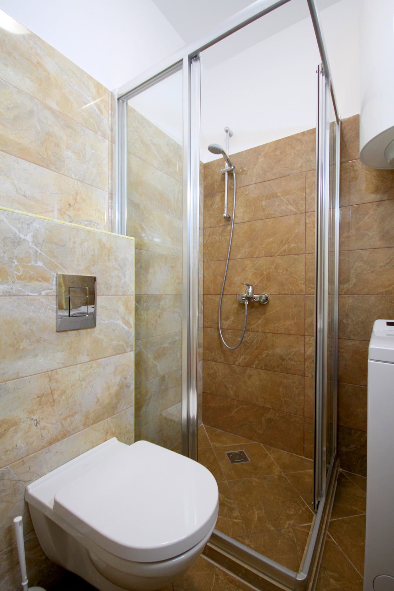 Modernes Badezimmer in einer Wohnung in Bečići, Montenegro: Duschkabine, Hänge-WC und beige Fliesen.