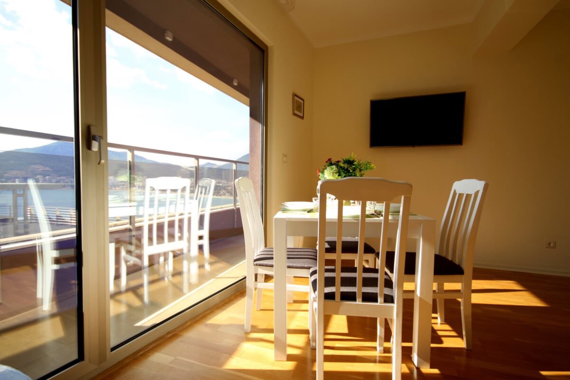 Wohnzimmer mit Essbereich und Panoramablick auf das Meer in einer Wohnung in Bečići, Montenegro. Helle Möbel und Terrasse.
