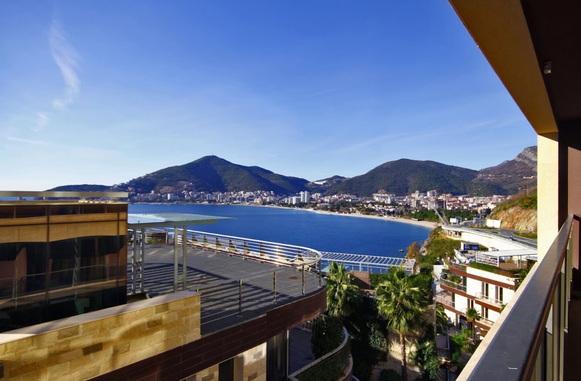 Blick vom Balkon einer Wohnung in Bečići, Montenegro: Panorama auf die Adria, den Strand und die Berge an einem sonnigen Tag.