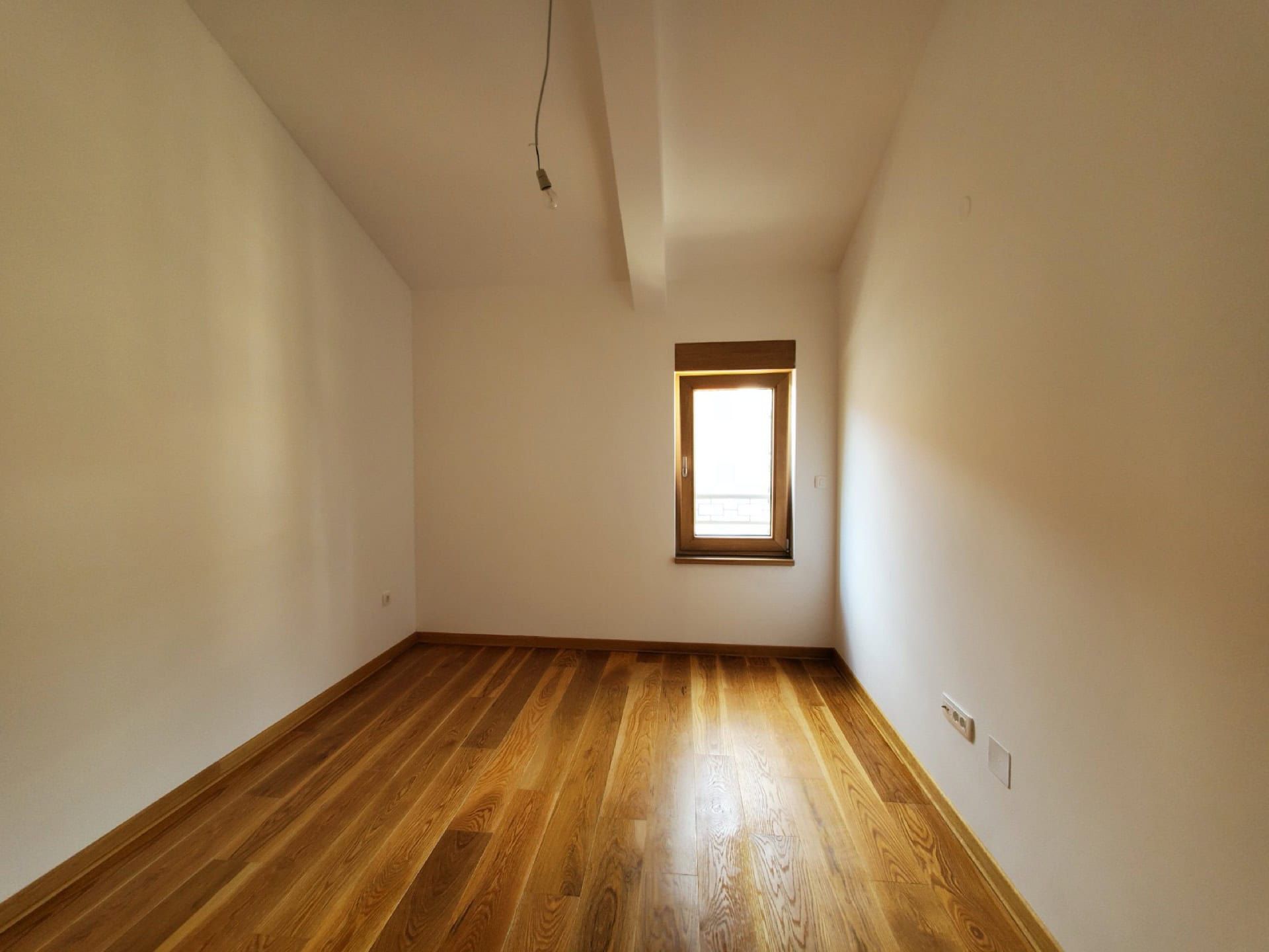 Bright bedroom with wooden floor and window in a penthouse, Pržno, Montenegro. Empty room with unfinished interior finish.