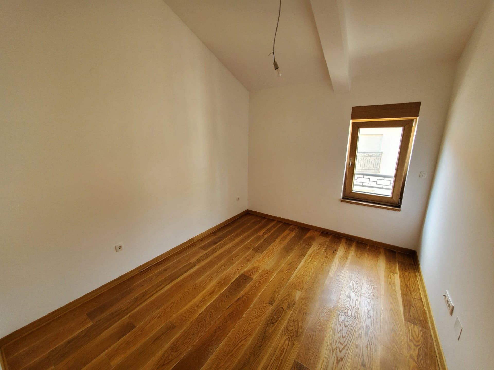 Bright bedroom with wooden flooring and a window in a penthouse, Pržno, Montenegro. Empty room with turnkey finishes.