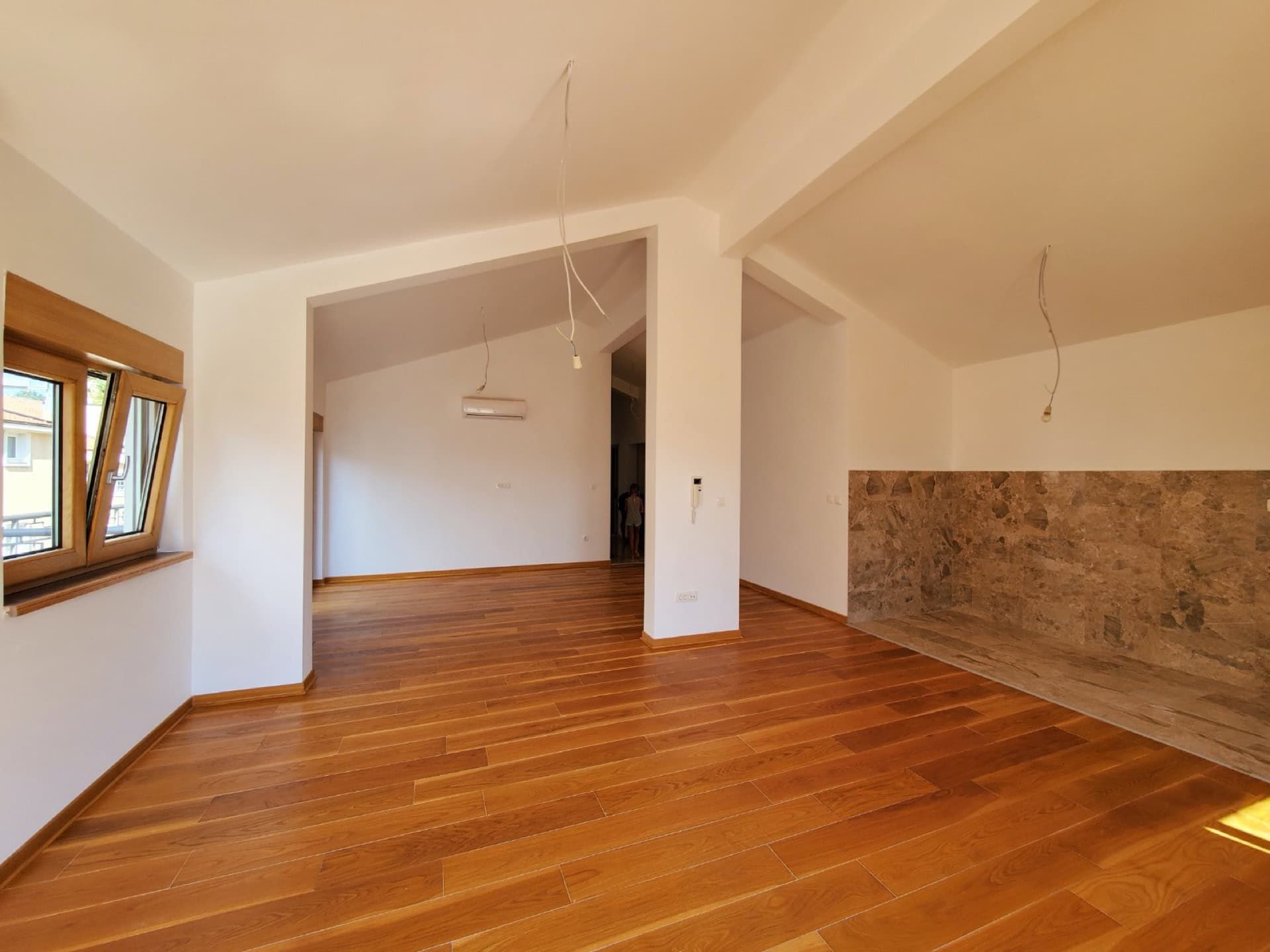 Bright living room in a penthouse in Pržno, Montenegro: wooden floor, stone accent wall, and panoramic window.