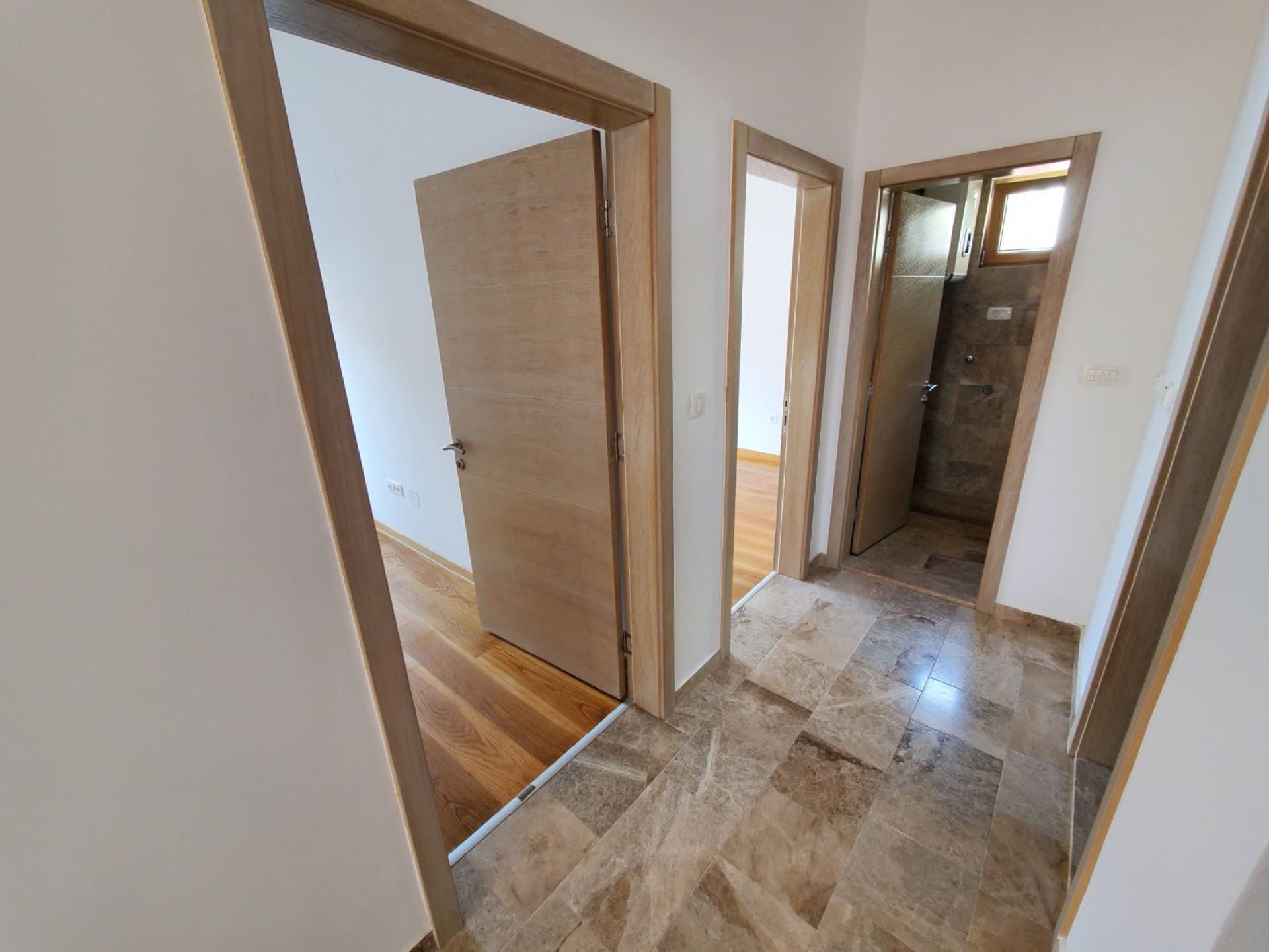 Hallway in a penthouse in Pržno, Montenegro: marble floor, light walls, and interior doors made of natural wood.