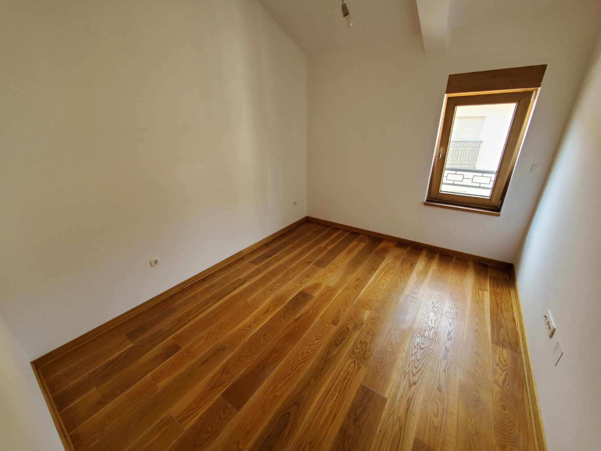 Bright bedroom with wooden flooring in a penthouse, Pržno, Montenegro. Empty room with a window and high-quality finishes.