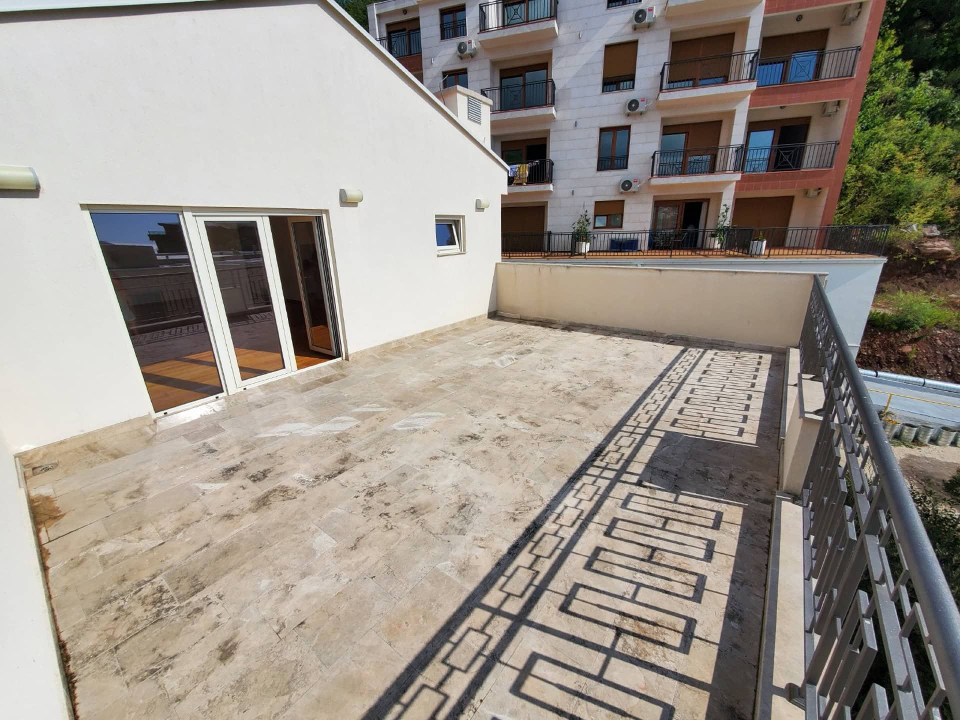 Spacious terrace with stone finishes in a penthouse, Pržno, Montenegro: view of the residential complex and panoramic doors.