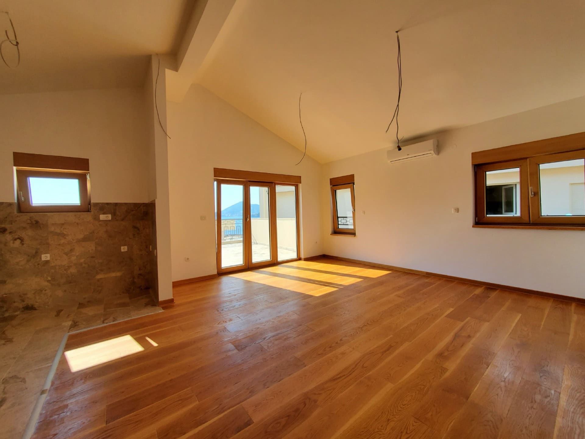 Bright living room in a penthouse, Pržno, Montenegro: parquet floor, panoramic windows with sea view and access to the terrace.