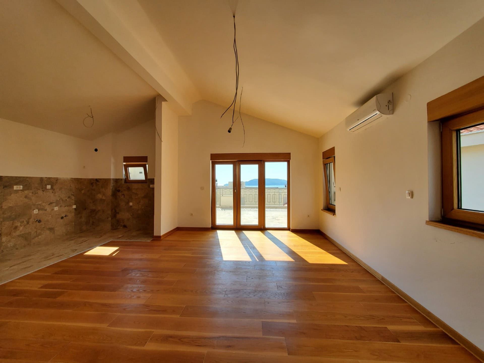 Bright living room in a penthouse in Pržno, Montenegro: parquet flooring, kitchen area, and access to a terrace with sea view.