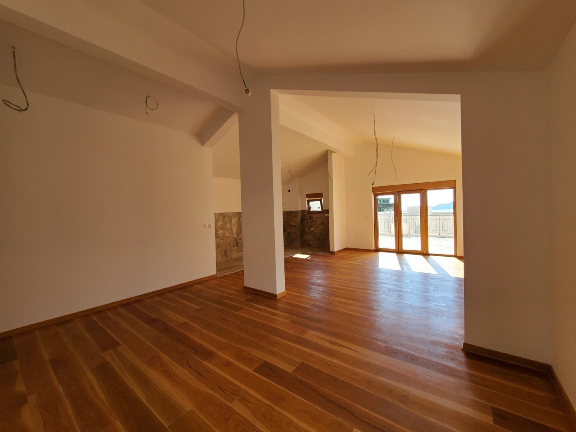 Spacious living room in a penthouse in Pržno, Montenegro: bright interior, wooden floor, and access to a terrace with a view.