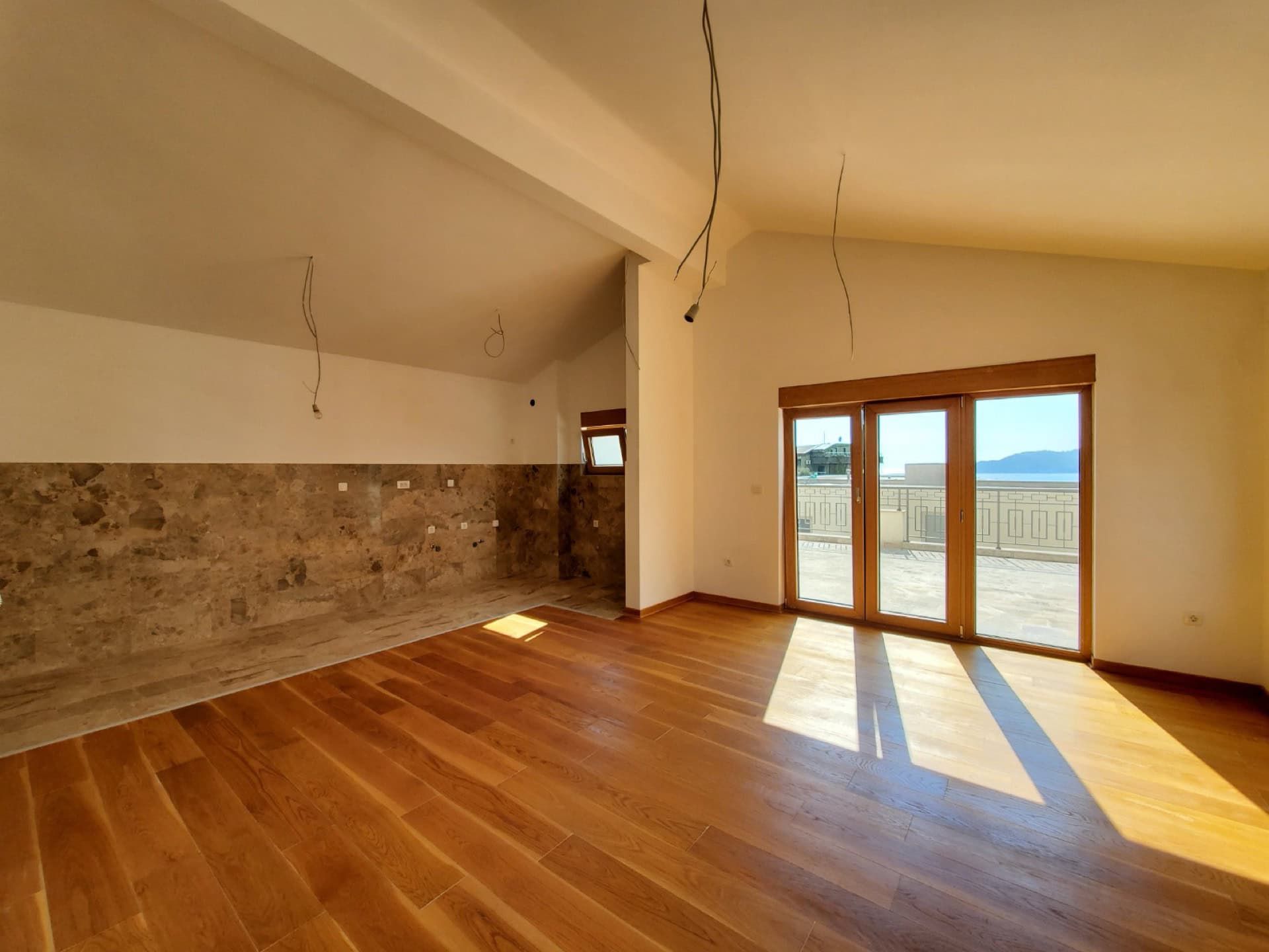 Living room in a penthouse in Pržno, Montenegro: parquet flooring, a kitchen area with stone finishes, and access to a terrace with a view.