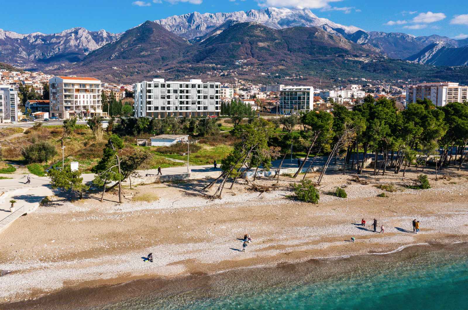Wohnanlage in Bar, Montenegro: Blick auf moderne Häuser am Meer, einen Kiesstrand und eine Berglandschaft im Hintergrund.