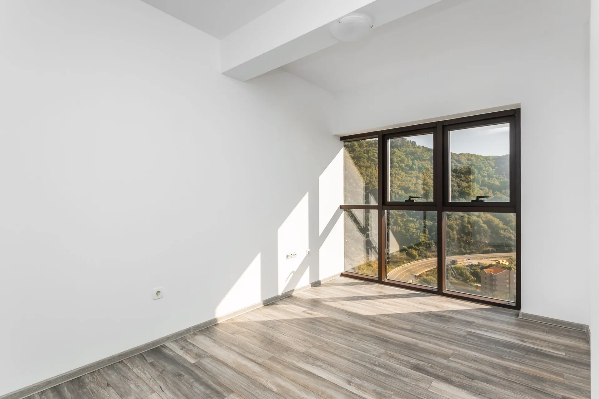 Helles Wohnzimmer im Penthouse, Rafailovići, Montenegro: Panoramafenster mit Bergblick und Holzoptik-Laminat.